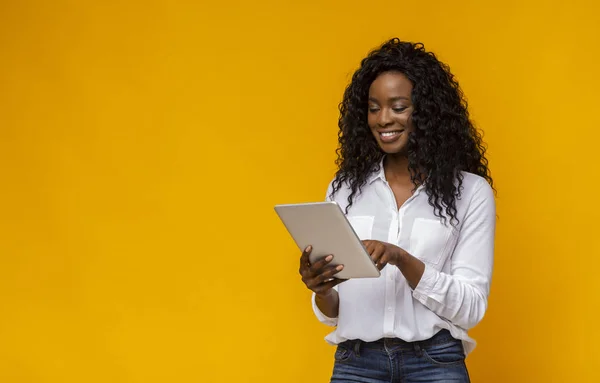 Interested african american girl using digital tablet on yellow background