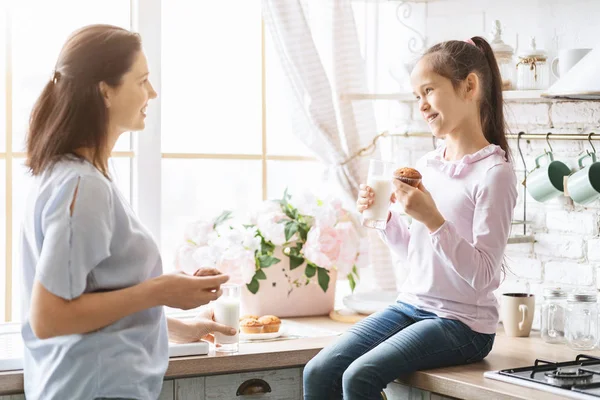 Маленька дівчинка їсть закуски і спілкується з мамою на кухні — стокове фото