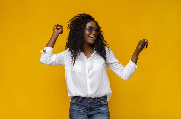 Mooie Afrikaanse vrouw met zonnebril dansen over gele achtergrond — Stockfoto