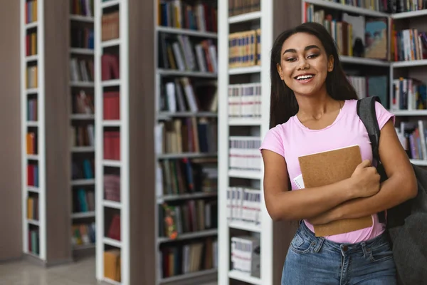 Весела студентка, що стоїть поруч з книжковими полицями — стокове фото