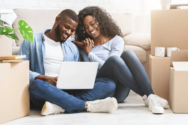 Pareja sonriente sentada en el piso en un apartamento nuevo, usando una computadora portátil —  Fotos de Stock