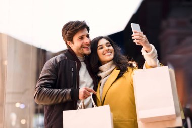 Şehir merkezinde alışveriş yaptıktan sonra selfie çeken genç çift