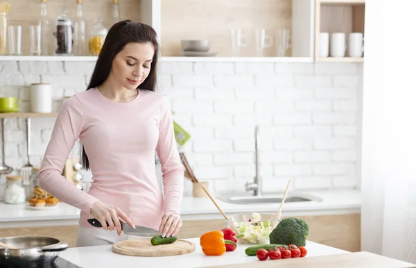 Ung kvinna skära färska grönsaker i köket — Stockfoto