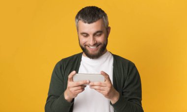 Sarı arka planda akıllı telefon kullanarak ilgilenen mutlu adam