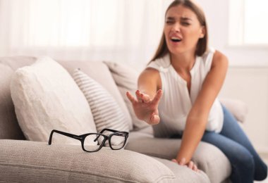 Girl Reaching For Eyeglasses Sitting On Sofa Indoor clipart