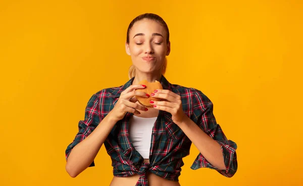 Ung kvinna äter hamburgare stående i studion — Stockfoto