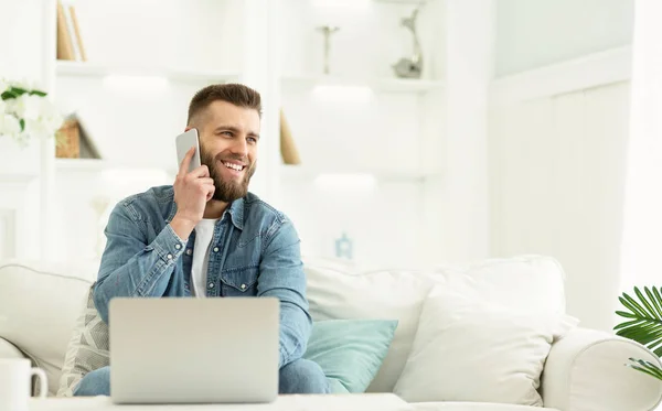 Homem feliz tendo conversa telefônica e trabalhando no laptop — Fotografia de Stock