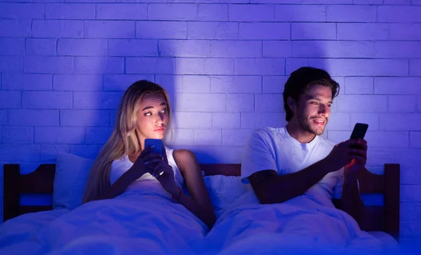 Infiel marido charlando en el teléfono móvil acostado con su esposa en la cama —  Fotos de Stock