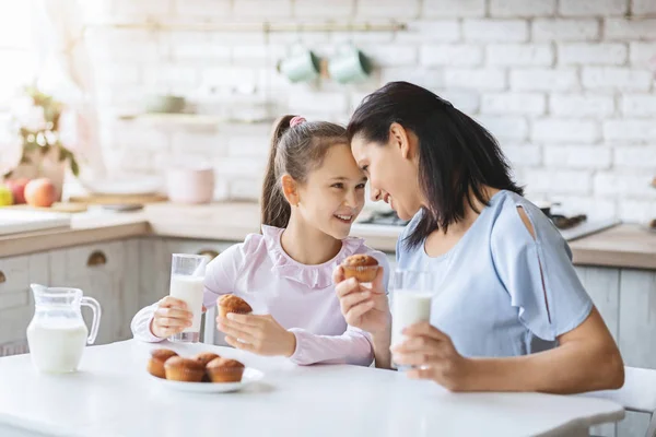 Mutter und Tochter essen Cupcakes und trinken Milch in der Küche. — Stockfoto