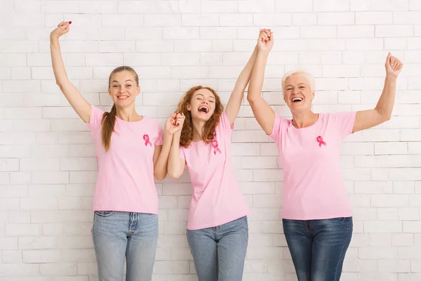 Tres mujeres usando camisetas de cáncer de mama sosteniendo las manos contra la pared — Foto de Stock