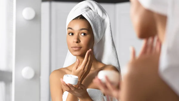 Dziewczyna trzyma twarz krem produkt nawilżający skóra w łazienka — Zdjęcie stockowe