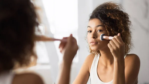 Afro mujer aplicando polvo facial con cepillo de maquillaje en el baño — Foto de Stock