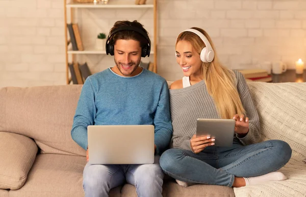 Pareja usando el ordenador portátil y la tableta sentada en el sofá en casa —  Fotos de Stock