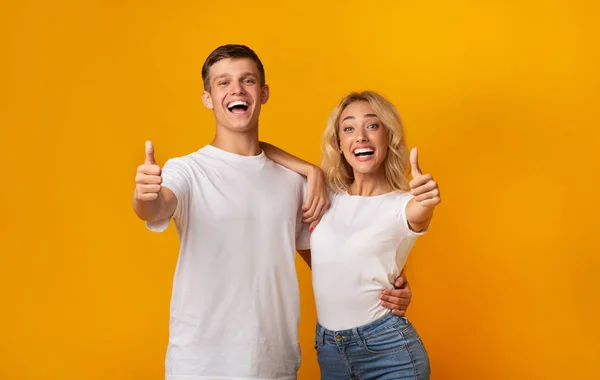 Jóvenes felices mostrando pulgares hacia arriba sobre fondo amarillo — Foto de Stock