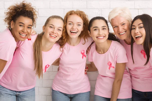 Mulheres com fitas de câncer de mama rosa rindo em fundo branco — Fotografia de Stock