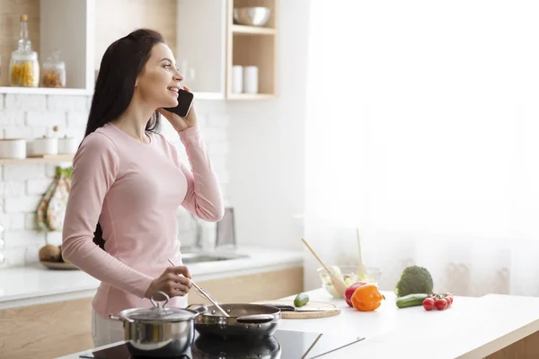 Millennial Frau telefoniert, bereitet Mittagessen in der Küche zu — Stockfoto