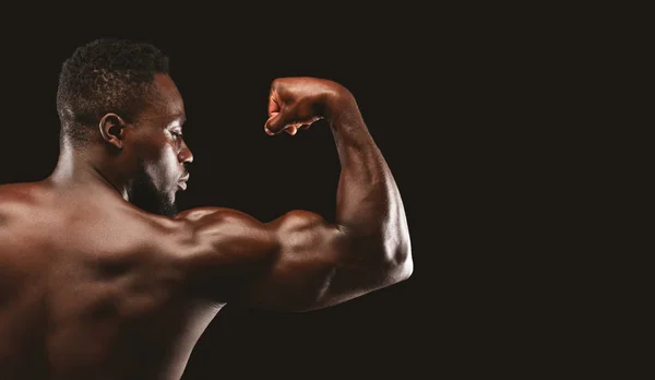 Afro-Bodybuilder zeigt starken Bizeps auf schwarzem Hintergrund — Stockfoto