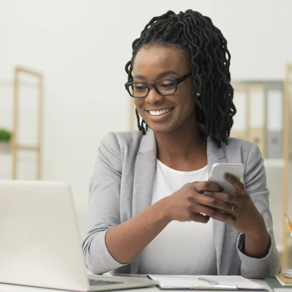 Afro empresária SMS via Smartphone sentado no escritório moderno — Fotografia de Stock