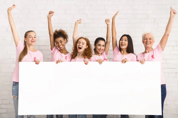 Camisetas de concienciación sobre el cáncer de mama de las señoras que sostienen el tablero en blanco en interiores —  Fotos de Stock