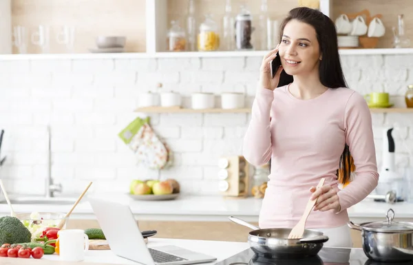 Jonge vrouw koken en praten op mobiele telefoon in de keuken — Stockfoto