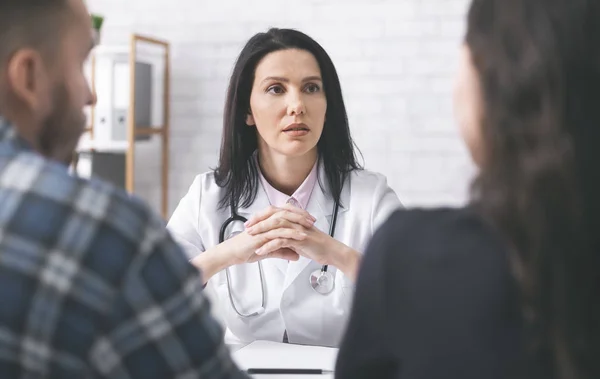 Doktor poslouchá pacienty, vysvětlující symptomy pro mladou rodinu — Stock fotografie