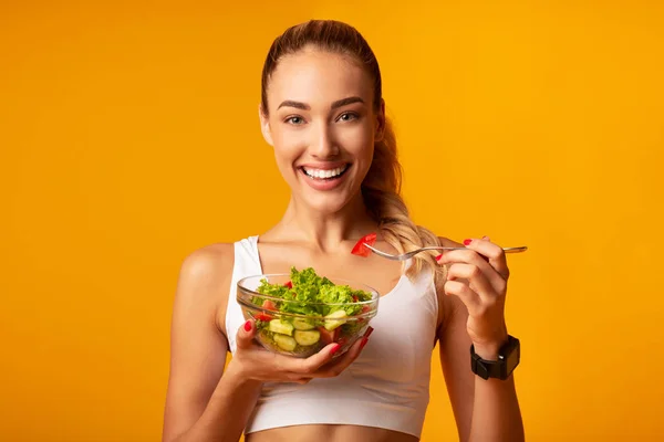 Fitness-Mädchen essen Gemüsesalat stehend über gelbem Hintergrund — Stockfoto