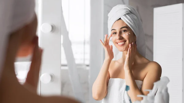 Mujer aplicando crema para los ojos cuidando de la piel en el baño —  Fotos de Stock