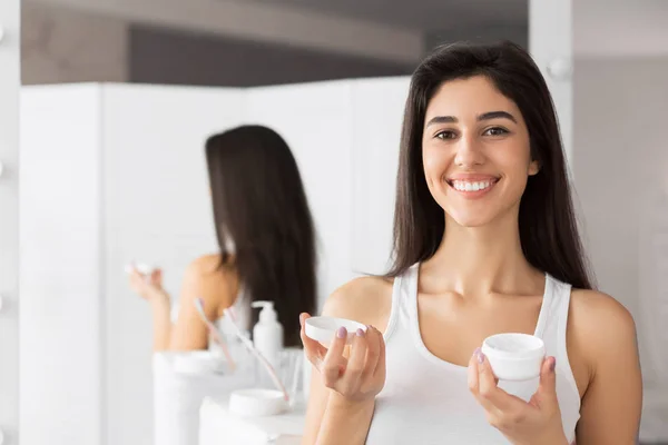 Jeune femme tenant visage crème produit debout dans la salle de bain — Photo