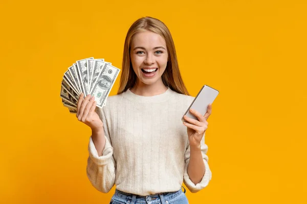 Ευτυχισμένος έφηβος κορίτσι δείχνει κρατώντας smartphone και ένα μάτσο χρήματα — Φωτογραφία Αρχείου