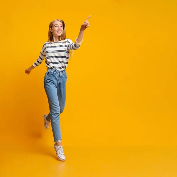 Chica alegre saltando y señalando en el espacio de copia en el fondo amarillo — Foto de Stock