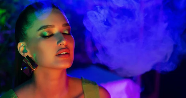 Young woman smoking vape in neon blue light — Stock Photo, Image
