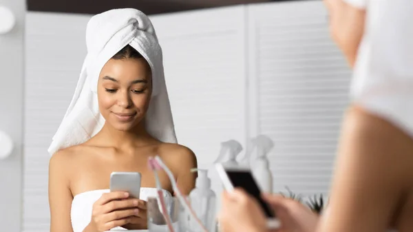 Mujer con toalla en la cabeza Mensajes de texto en el teléfono inteligente en el baño — Foto de Stock
