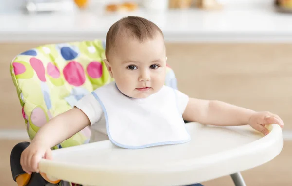 Cute baby boy sitting in high children chair in kitchen — Stock Photo, Image