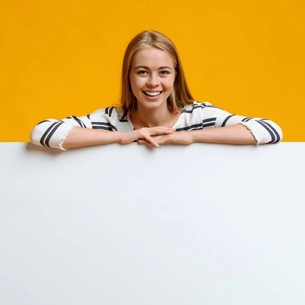 Lachende tiener meisje leunend op blanco wit bord — Stockfoto