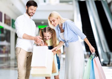 Alışveriş merkezinde eşi ve kızına alışveriş poşetleri gösteren adam