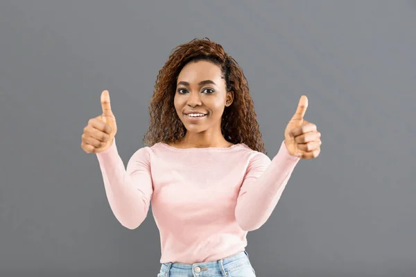 Chica alegre mostrando pulgares hacia arriba sobre fondo gris — Foto de Stock