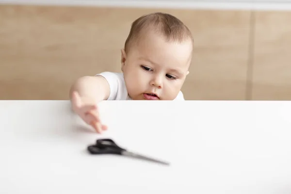 Baby pojke försöker få sax från köksbordet — Stockfoto