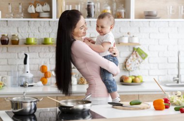 Küçük bebek anne ellerinde gülüyor, mutfakta