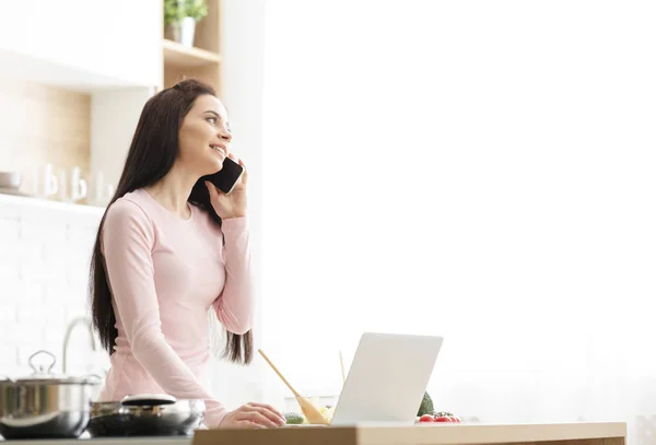 Duizendjarige vrouw werken thuis, praten over telefoon in de keuken — Stockfoto