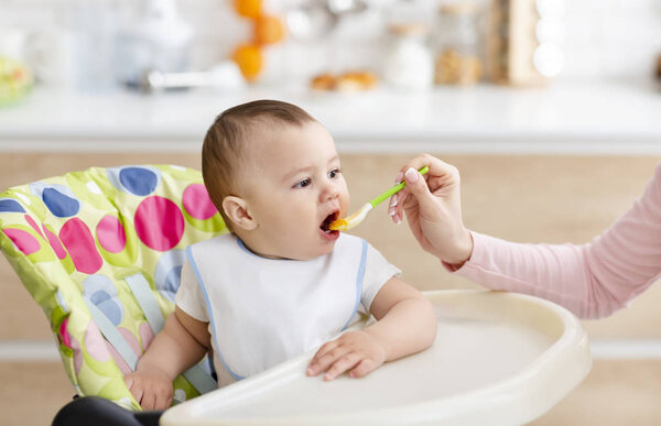 Mother giving healthy food to her adorable son at kitchen