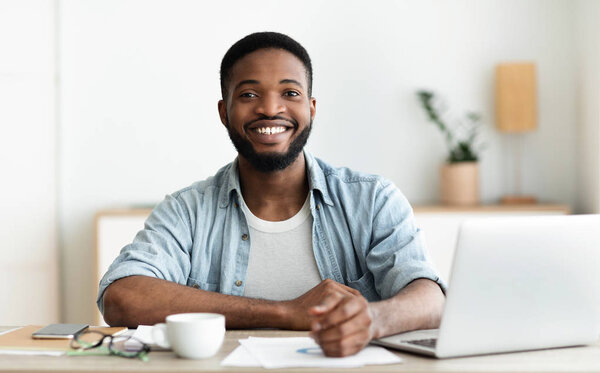 Positive black guy posing to camera at workplace
