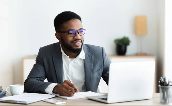 Empreendedor preto bonito trabalhando no laptop e tomar notas — Fotografia de Stock