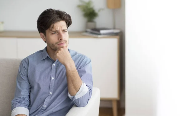 Uomo solitario che pensa di toccare il mento seduto sul divano al coperto — Foto Stock