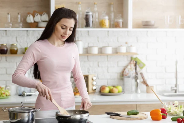 Jonge vrouw bereidt maaltijd op fornuis thuis — Stockfoto