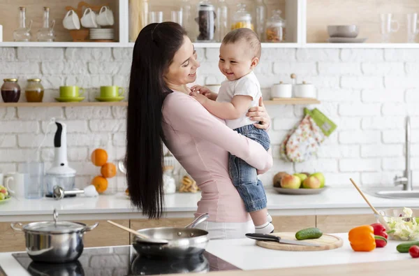 Petit bébé riant sur les mains de la mère, dans la cuisine — Photo