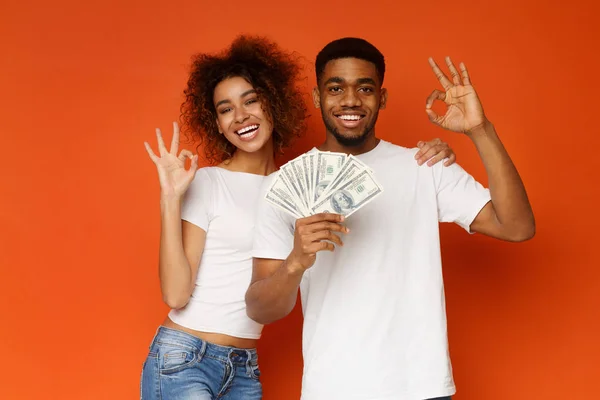 Happy african man and woman gesturing OK sign with lots of money