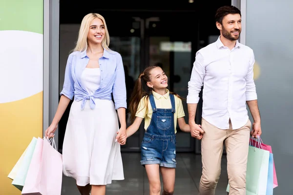 Familia de tres dejando el centro comercial llevando bolsas —  Fotos de Stock