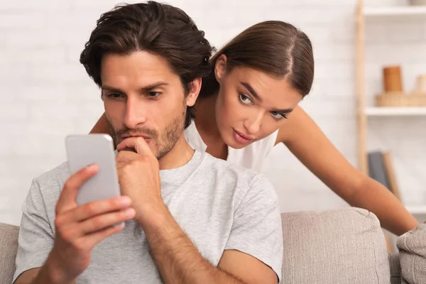 Jaloerse vrouw bespioneren man terwijl hij texting op telefoon indoor — Stockfoto