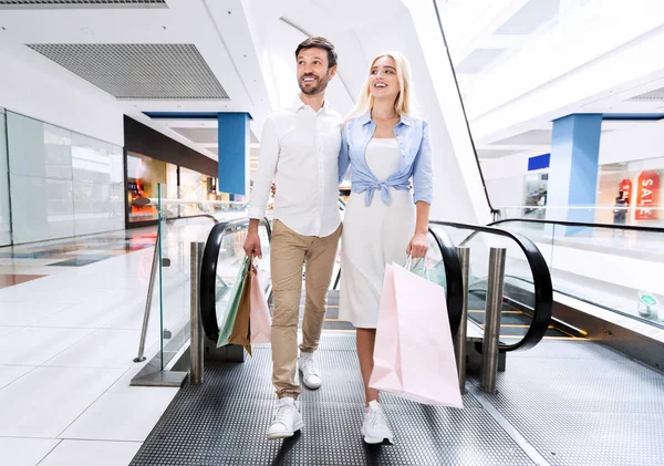 Οι σύζυγοι κάνουν τα ψώνια να πάρει από κυλιόμενες σκάλες κρατώντας σακούλες σε εμπορικό κέντρο — Φωτογραφία Αρχείου