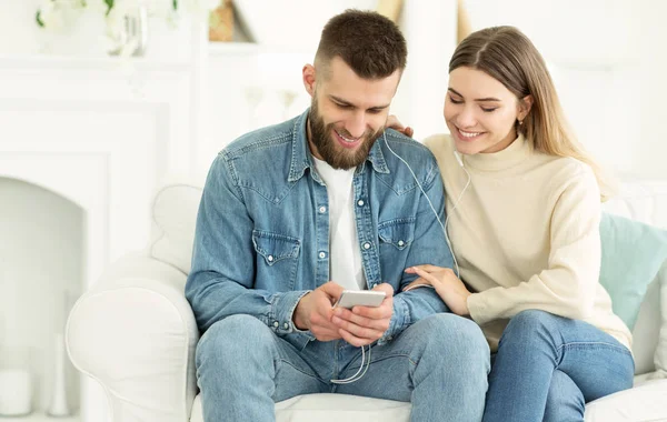 Happy couple sharing music from smartphone sitting on couch